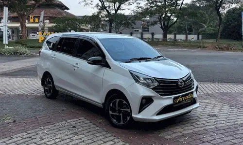 mobil Daihatsu Sigra warna putih metalik tahun 2023 di jalanan dealer. Mobil MPV LCGC 7 penumpang dengan velg two-tone.