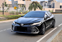 Toyota Camry warna silver difoto dari sudut depan samping, menampilkan desain sedan eksekutif dengan grille depan besar bergaya sporty, headlamp LED tajam, garis body yang mengalir elegan, dan velg alloy multi-spoke. Sebagai armada premium sewa mobil di Medan, Camry menjadi pilihan sedan mewah untuk kebutuhan protokoler, wedding car, jemputan tamu VIP/eksekutif perusahaan, hingga perjalanan bisnis yang mengutamakan kenyamanan dan kesan formal-elegan.