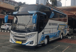 Medium bus/bus sedang warna biru dengan aksen garis kuning-putih bergelombang di bagian bodi, difoto dari sudut depan samping, menampilkan kaca jendela lebar berjejer di sepanjang kabin dan desain bus pariwisata dengan kapasitas menengah. Sebagai armada sewa bus di Medan, medium bus ini menjadi pilihan tepat untuk rombongan sedang seperti study tour sekolah, gathering perusahaan, ziarah/wisata religi, hingga perjalanan wisata rombongan ke Danau Toba dan Berastagi dengan kapasitas sekitar 25-31 seat, lebih besar dari Hiace namun lebih fleksibel dari big bus.