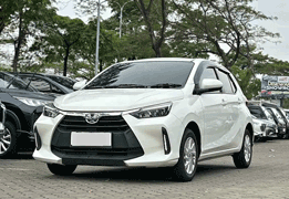 Toyota Agya GR Sport warna putih difoto dari sudut depan samping, menampilkan desain city car terbaru dengan grille depan trapesium tajam ala GR Sport, headlamp LED sipit modern, dan velg alloy hitam sporty. Sebagai armada ekonomis sewa mobil di Medan, Agya menjadi pilihan tepat untuk perjalanan dalam kota, solo traveler, pasangan, atau keluarga kecil yang mengutamakan efisiensi bahan bakar dan kemudahan parkir di area padat seperti pusat kota Medan.